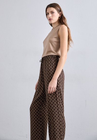 Beige ermeløs topp kombinert med brune mønstrede vide bukser med snøring i livet og geometriske design i lysere toner.