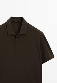 Mörkbrun polo tröja med krage och tre knappar. Tillverkad av texturerat tyg, med korta ärmar och minimala sömnadsdetaljer.