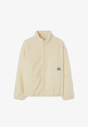 Giacca in pile color crema con zip sul davanti, colletto alto e tasche laterali. Presenta una piccola etichetta multicolore del marchio sul lato sinistro del petto.