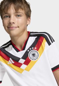 Tysk landslagströja i vitt med diagonala ränder i svart, rött och gult, svart krage och en rund logotyp med en örn.