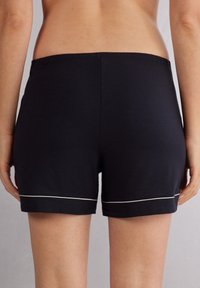 Tmavě modré bavlněné šortky s elastickým pasem, s bílou akcentní linií blízko lemu. Hladká textura s jednoduchým designem.