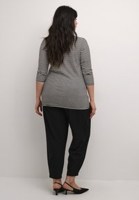 Top de manga larga de rayas blancas y negras combinado con pantalones negros de corte holgado y zapatos de tacón bajo tipo slingback en negro.