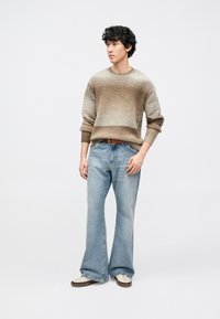 Brun och beige stickad tröja med rund hals och långa ärmar, kombinerad med ljusblå jeans med vida ben och cremefärgade sneakers.