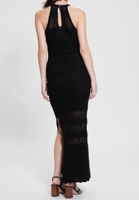 Robe longue noire sans manches avec un dos échancré en forme de clé, réalisée en tissu en maille texturée avec des motifs horizontaux et une fente latérale.