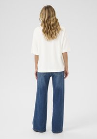 White short-sleeve t-shirt and wide-leg blue jeans. T-shirt features a straight hem; jeans have a faded wash with back pockets.