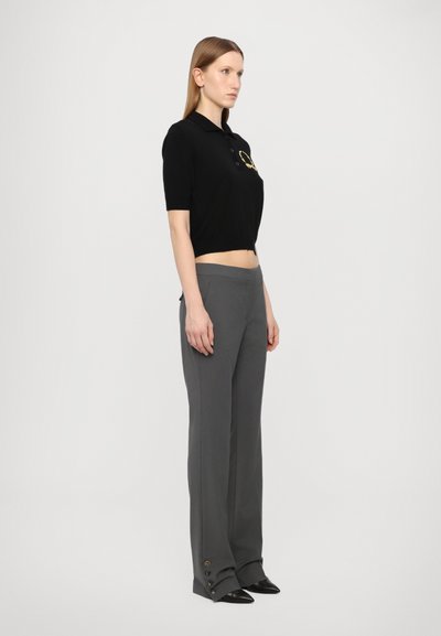 Polo shirt negru scurt cu mâneci scurte și logo auriu, asortat cu pantaloni gri cu picioare late, având nasturi pe laterale.