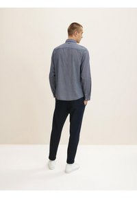 Conjunto casual para hombre: camisa de botones a rayas en azul marino y pantalones oscuros. La camisa cuenta con un collar clásico y mangas largas. Unas zapatillas blancas completan el look.