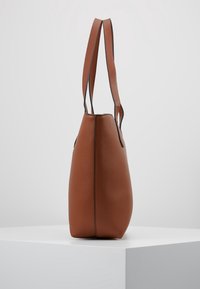 Hnědá kožená taška přes rameno s hladkým povrchem, zúženým tvarem a dvěma dlouhými popruhy. Má kontrastní černé lemování podél švů.