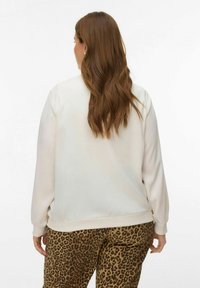 Sweat-shirt beige clair à manches longues et coupe décontractée, associé à un pantalon marron à imprimé léopard avec une ceinture élastique et des poignets élastiques.