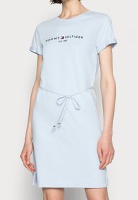 Jasnoniebieska sukienka z krótkim rękawem, z podwiniętymi mankietami, regulowanym paskiem w talii oraz logo "Tommy Hilfiger EST. 1985" na klatce piersiowej.