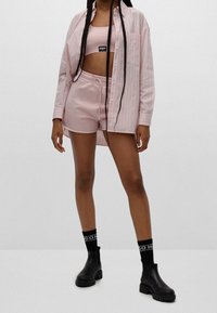 Růžová pruhovaná košile přes odpovídající růžový tílko a kraťasy. Černé kotníkové boty a ponožky s bílým brandingem. Hladký materiál, uvolněný střih.