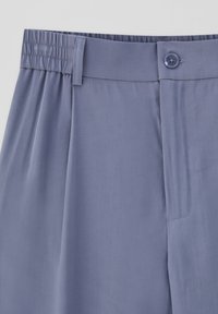 Ljust lila byxor i en texturerad tyg, med flat framsida, elastisk midjeband och enkel knappstängning.