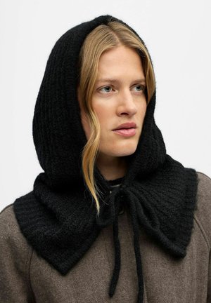 Sciarpa nera lavorata a maglia con cappuccio e un ampio colletto, caratterizzata da un tessuto testurizzato e una chiusura a legatura al collo, indossata sopra un indumento marrone.