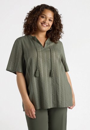 Blusa verde oliva con maniche corte, tessuto testurizzato, righe verticali e doppi pom-pom al colletto. Abbinata a pantaloni coordinati.