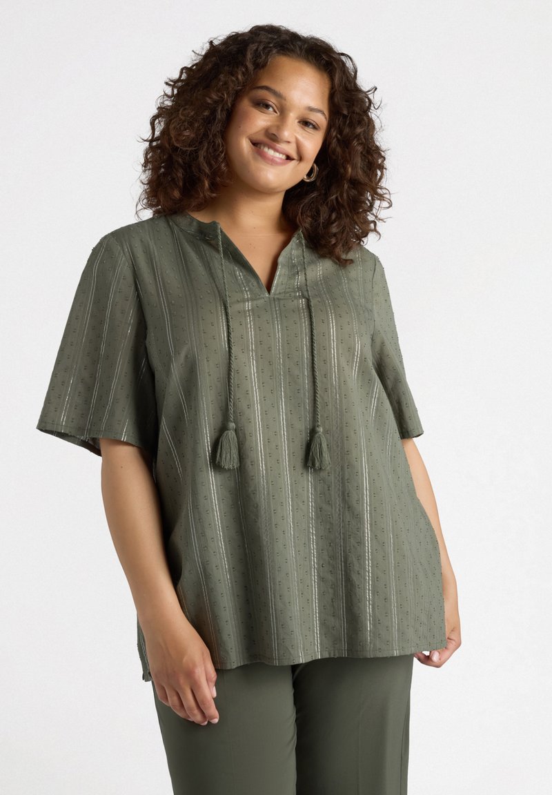 Blusa verde oliva con mangas cortas, tela texturizada, rayas verticales y dos borlas en el escote. Combina con pantalones a juego.