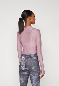 Helles pinkes langärmliges Sportoberteil mit Netzabschnitten und einem Logo. Kombiniert mit dunklen, gemusterten Leggings mit einem von der Galaxie inspirierten Design.
