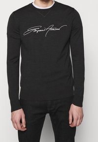 Dark gray long-sleeve sweater in soft fabric featuring a white script logo across the chest. Rounded neckline and ribbed cuffs and hem.