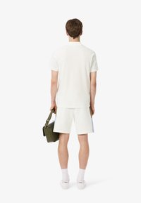 Un t-shirt blanc en coton à col rond et un short assorti, accompagnés d'un sac à bandoulière vert. La chaussure est blanche avec des accents subtils.