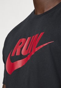 Μαύρη βαμβακερή μπλούζα t-shirt με έντονο σχεδιασμό "RUN" σε κόκκινο χρώμα και το λογότυπο της Nike, με κοντά μανίκια και στρογγυλή λαιμόκοψη.