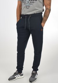 Navy joggers with a fitted design, elastic waistband, drawstring closure, and logo patch. Features side pockets and ribbed cuffs.