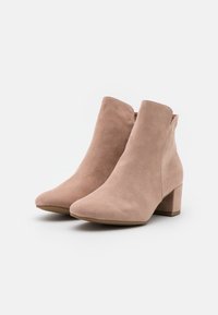 Beige Wildleder-Stiefeletten mit runder Zehenform und einem mittellangen Blockabsatz. Mit seitlichen Reißverschlüssen und minimalen Nahtdetails.