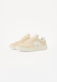 Sneaker in maglia beige con accenti bianchi; punta tonda, suola piatta e design con lacci. Tessuto текстurizzato con un aspetto traspirante.