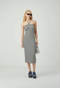 Μίντι φόρεμα με ρίγες και λαιμόκοψη halter, με μαύρες και λευκές ρίγες. Συνδυασμένο με μπλε πλατφόρμες παπούτσια και κρατώντας μια μικρή τσάντα.