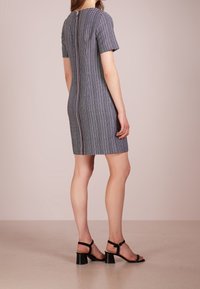 Rukávový, přiléhavý šaty v námořnické modři s kostkovaným vzorem, s viditelným středním zipem na zadní straně a hladkou texturou látky.