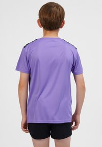 Kortärmad lila sporttröja med en slät textur och svarta detaljer på axlarna, kombinerad med svarta shorts.