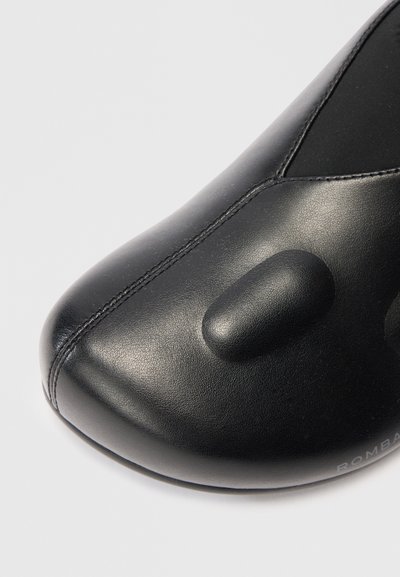 Scarpa in pelle nera con punta arrotondata, superficie liscia e cuciture evidenti. Include dettagli imbottiti e il nome del marchio "ROMBA."