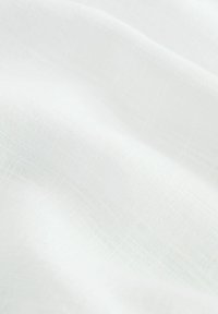 Detailní záběr na jemnou, bílou tkaninu s jemnou strukturou a měkkými záhyby, která zdůrazňuje jemné vlákna a prodyšný materiál.