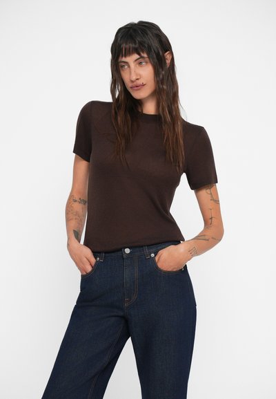 Camiseta de manga corta marrón con cuello redondo, combinada con jeans oscuros con costuras claras y bolsillos frontales.
