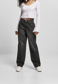 Top corto de color púrpura claro con botones, combinado con unos jeans de mezclilla oscuros de pierna ancha de cintura alta. Zapatillas blancas completan el atuendo.