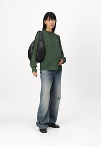Zeleni teksturirani dugosleeve top, oversized svijetloplave traperice, crna torba i crne cipele. Jednostavan dizajn s opuštenim krojem i vidljivim šavovima.
