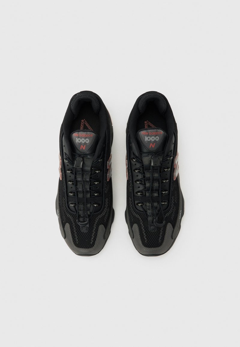 Par de zapatillas negras New Balance 1000 con detalles de malla y cuero, con cordones y acentos en rojo del logo, vistas desde arriba sobre un fondo gris.