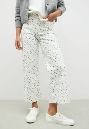 Pantaloni scurți, cu picioare largi, dintr-un material alb cu un imprimeu floral albastru mic. Stilizați cu un cardigan gri și adidași albi.