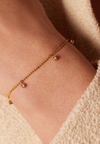 Gouden armband met kleine ronde kralen en twee heldere kristalaccenten, met een verfijnd kettingontwerp en een gladde, glanzende textuur.