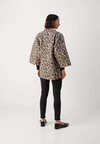 Leopardenmuster, übergroße Jacke mit Dreiviertelärmeln, schwarzem Besatz und abgerundetem Saum, kombiniert mit schwarzen, figurbetonten Hosen und Ballerinas.