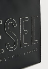 Borsa tote nera con logo "DIESEL" in rilievo e testo "SUCCESSFUL LIVING", caratterizzata da una texture opaca liscia e bordi cuciti.
