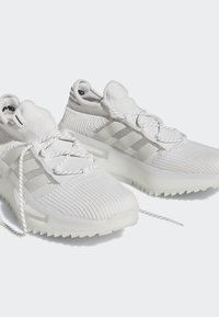 Pantofi sport albi cu un superior din tricot texturat, accente reflective și o talpă din cauciuc. Prezintă șireturi și o talpă căptușită pentru confort.