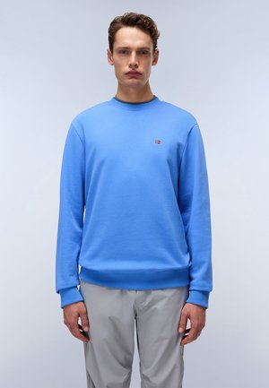 Light blue crew neck sweatshirt made of textured fabric. Features a small logo on the chest and ribbed cuffs and hem. Paired with light gray pants.