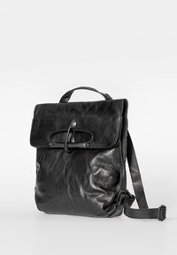 Musta nahkainen reppu, jossa on yläkahva, läppäkiinnitys lenkillä ja napilla sekä säädettävä olkahihna, yksinkertaisella taustalla.