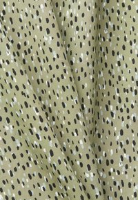 Světlá olivově zelená látka s nepravidelným malým černým, bílým a šedým skvrnitým vzorem, vykazující záhyby a jemnou texturu.