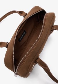 Sac à main en daim marron avec fermeture éclair, texture lisse, intérieur organisé et accents en métal sur les côtés.