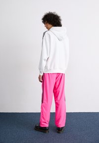 White hooded sweatshirt, pink track pants with black side stripes, and black platform shoes. The texture appears smooth and casual.