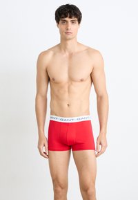 Rote Baumwoll-Boxershorts mit einem weißen elastischen Bund, der das "GANT"-Logo trägt. Glatte Textur, figurbetontes Design und Oberschenkel-lange.
