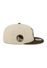 Cremefarbener Snapback-Cap mit braunem Schirm, versehen mit einem gestickten, runden Logo und verstellbarem Verschluss auf der Rückseite.