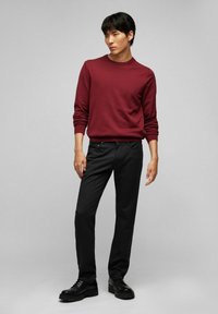 Pull en maille bordeaux, avec un col rond et des manches longues, associé à un pantalon noir texturé. Chaussures : bottes noires à lacets avec une semelle épaisse.