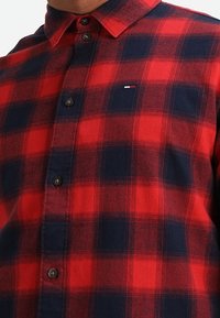Chemise à carreaux rouge et marine en tissu flanelle, dotée d'un col à bouton, de boutons sur le devant et d'un logo brodé sur la poitrine.