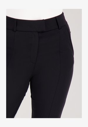 Close-up van zwarte, getailleerde broek met riemlussen en een verborgen sluiting aan de voorkant op een witte achtergrond.